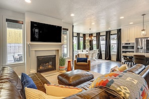 A modern living room with a fireplace, leather sofas, a flat-screen TV, and a dining area with a view. - Hot Tub, Group Hub, Close to Deer Valley (Heber City)