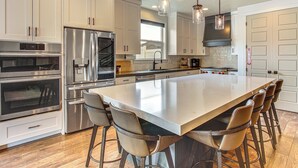 A modern kitchen with stainless steel appliances, a large island with bar stools, and pendant lighting. - Hot Tub, Group Hub, Close to Deer Valley (Heber City)