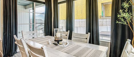 Un comedor con una mesa grande, sillas, una araña y vistas al exterior.