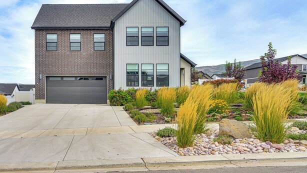 A two-story house with a garage, a landscaped front yard with various plants, and a clear sky. - Hot Tub, Group Hub, Close to Deer Valley (Heber City)