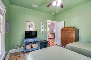 Ein Zimmer mit grünen Wänden, einem Deckenventilator, einem blauen Schminktischchen mit Fernseher, einem Holzschrank und einem Bett mit grüner Bettwäsche.
