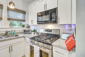 Une cuisine moderne avec des meubles blancs, des appareils en acier inoxydable, une cuisinière à gaz, un four à micro-ondes et un grille-pain.