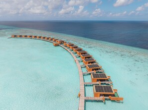 Eine Reihe von überwasserbungalows, die durch einen Holzsteg mit dem klaren, türkisblauen Meer verbunden sind.