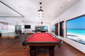 A pool table with a red felt surface, wooden legs, and a pool cue rack. - Veligandu Island Resort & Spa (Veligandu Island)