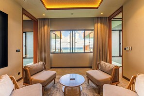 Ein Hotelzimmer mit großem Fenster und Meerblick, zwei Sofas, einem kleinen runden Tisch und einer Deckenleuchte.