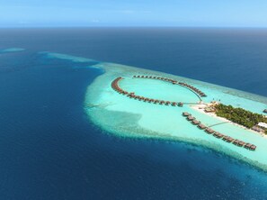 Eine Luftaufnahme eines Resorts mit überwasserbungalows, die in einem Halbkreis um eine zentrale Lagune angeordnet sind.