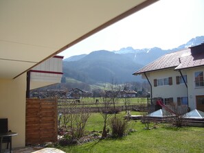 A covered outdoor area with a view of a mountain range, a wooden fence, and a building with a tiled roof. - 95-square-meter vacation rental with a separate bedroom and a terrace on the ground floor (Aschau im Chiemgau)
