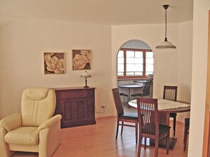 A dining area with a round table, chairs, a wooden cabinet, and two wall-mounted flower paintings. - 95 m² Vacation Rental with Separate Bedroom and Ground-Floor Terrace (Aschau im Chiemgau)