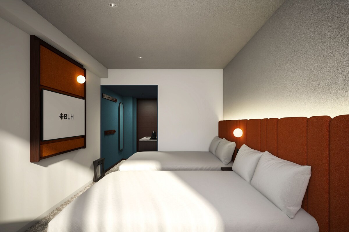 Habitación de hotel con dos camas, cabecera de madera, un cartel enmarcado en la pared y una puerta que da a un baño.