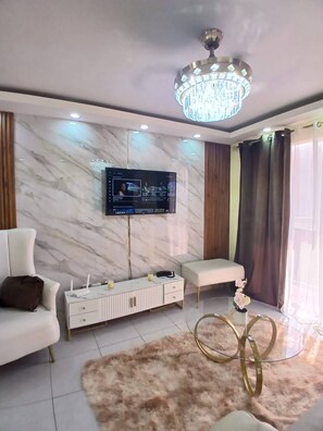 Ein modernes Wohnzimmer mit Marmorwand, einem Wand-Fernseher, einem weißen Sofa, einem Glastisch und einer Kristallleuchtre.