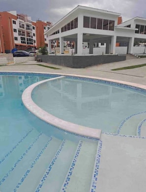 Ein Pool mit geschwungener Kante und blauen Fliesen, umgeben von einem Gebäude mit flachem Dach und großen Fenstern.