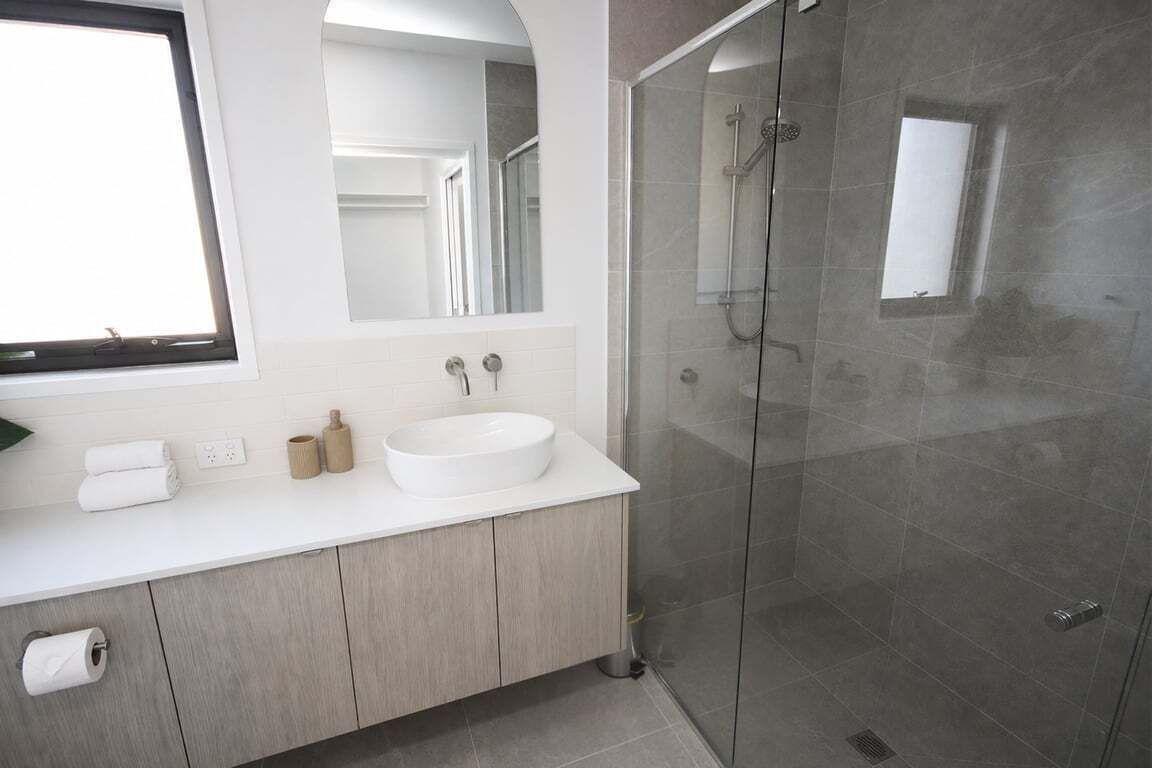 Une salle de bain moderne avec un meuble-lavabo blanc, un grand miroir, une douche à parois de verre et une fenêtre.