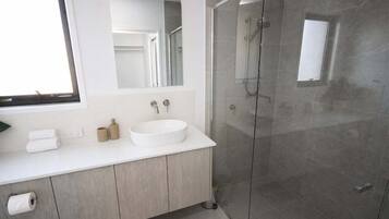 Une salle de bain moderne avec un meuble-lavabo blanc, un grand miroir, une douche à parois de verre et une fenêtre.