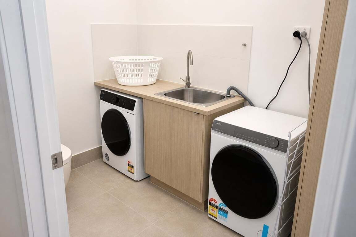 A compact laundry area with a washing machine, a dryer, a sink, and a basket.