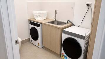 A compact laundry area with a washing machine, a dryer, a sink, and a basket.