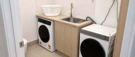 A compact laundry area with a washing machine, a dryer, a sink, and a basket.