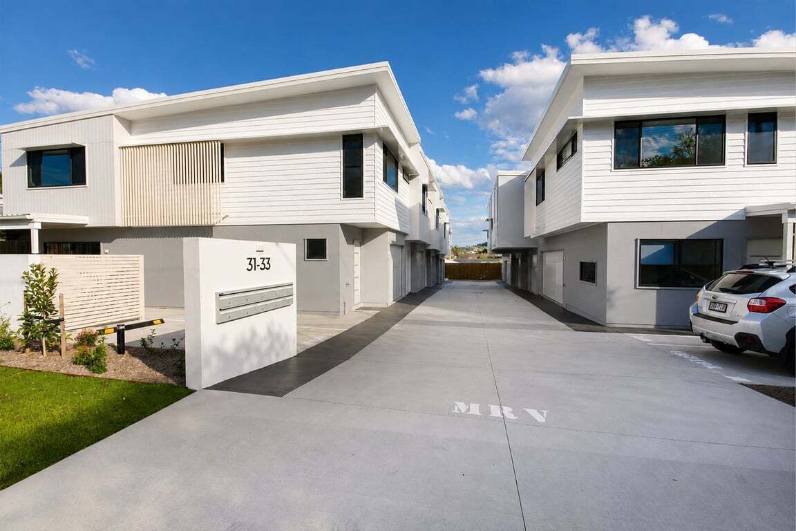 A modern residential building with a clean, minimalist design, featuring a driveway and a parked car.