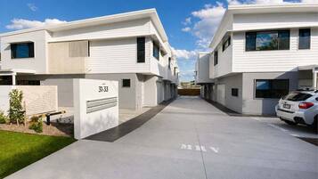 A modern residential building with a clean, minimalist design, featuring a driveway and a parked car.