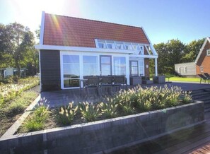 Uma casa moderna com uma grande janela de vidro, fachada de tijolos e um alpendre com mobiliário para área externa.
