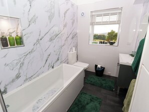 Ein Badezimmer mit Marmorwand, einer Badewanne, einem Waschbecken, einem Fenster mit Blick und grünen Teppichen.