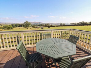 Eine Holzterrasse mit Tisch und Stühlen mit Blick auf eine Wiese mit Kühen.