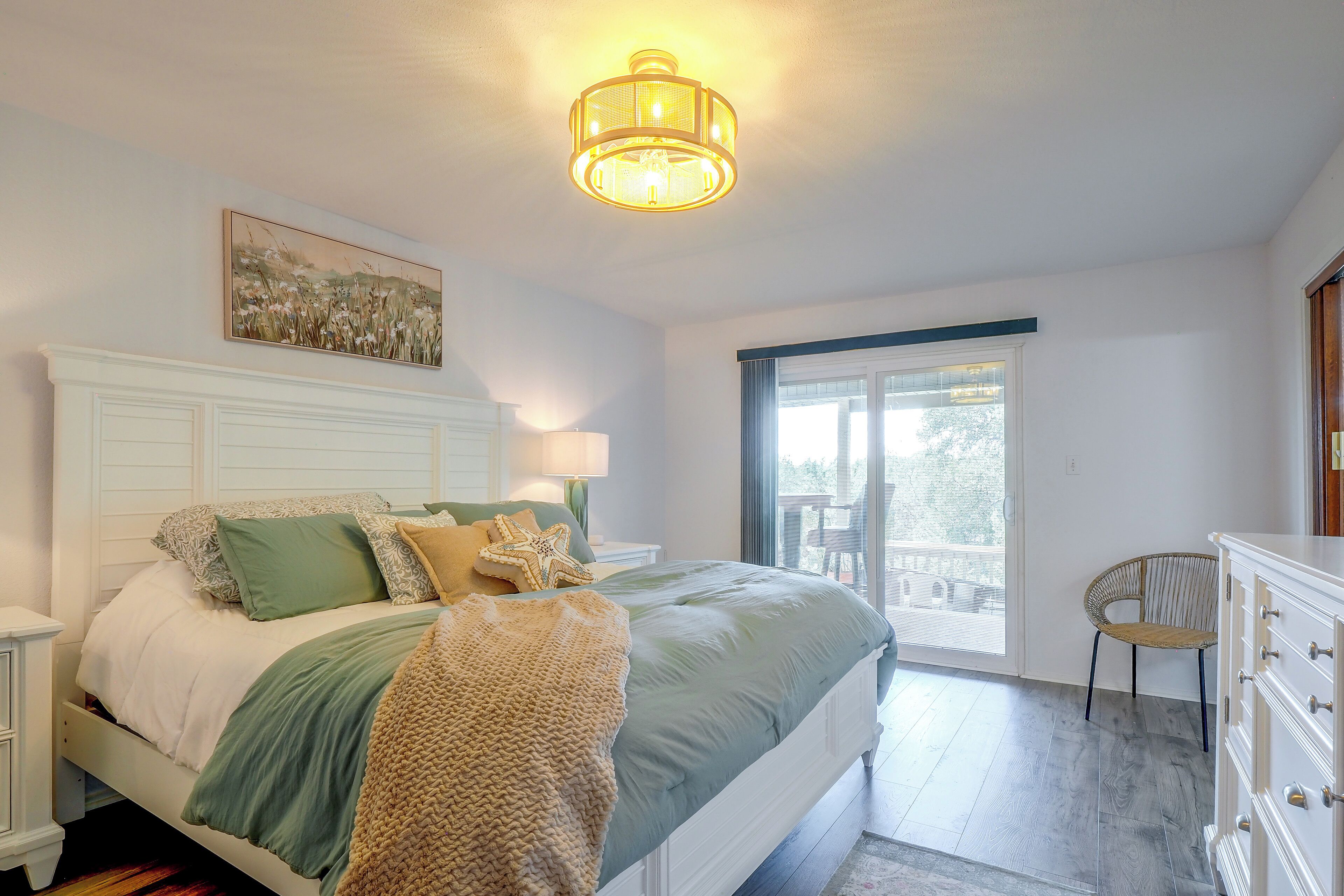Une chambre à coucher comprenant un lit, une table de chevet, une lampe, un coussin en forme d’étoile de mer, un tableau, une chaise et une commode.