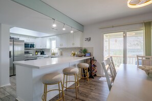 A modern kitchen with a central island, bar stools, and a dining area with a view. - Private Dock, Lake-View Deck! Point Venture Home (Leander)