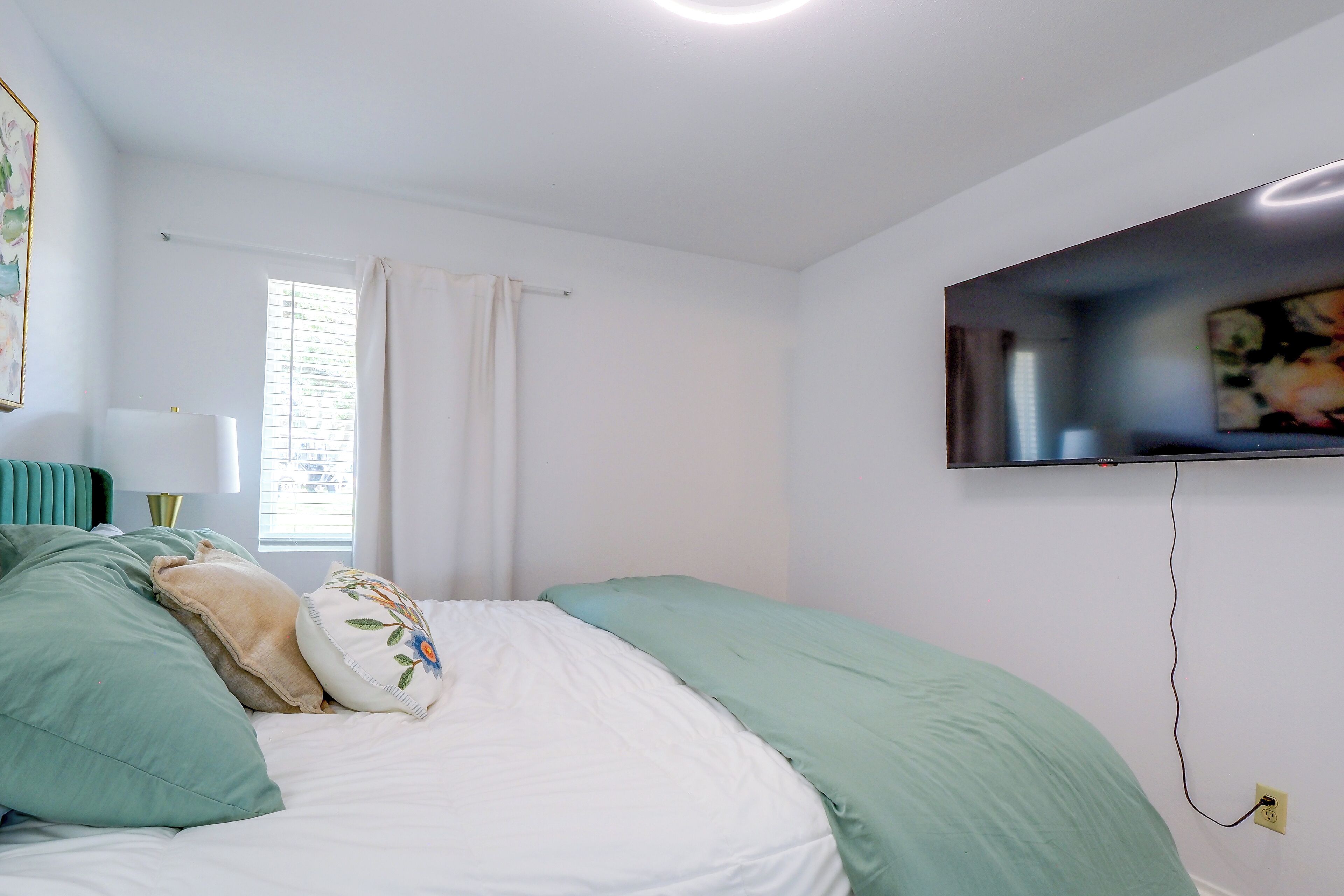 A bedroom with a bed, a television mounted on the wall, and a window with curtains.