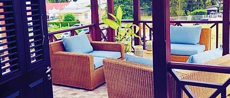 An outdoor covered seating area with wicker furniture and a potted plant.