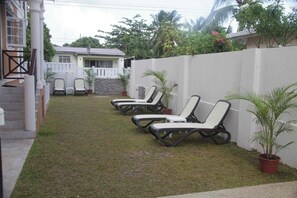 A backyard with a white wall, a small garden, and a row of lounge chairs. - Panthera Terra #4 - By ZenBreak (Mount Standfast)