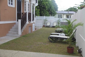 A residential area with a white fence, a small lawn, and outdoor furniture. - Panthera Terra #4 - By ZenBreak (Mount Standfast)