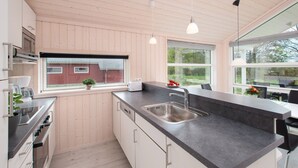 A modern kitchen with wooden paneling, a built-in oven, a sink, and pendant lighting. - Nordic House With Sauna (Grossenbrode)