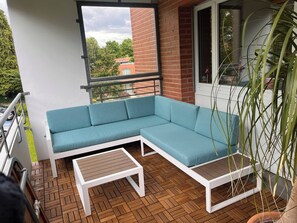 Un balcón con un sofá seccional azul, una mesita de centro blanca y una planta en maceta.