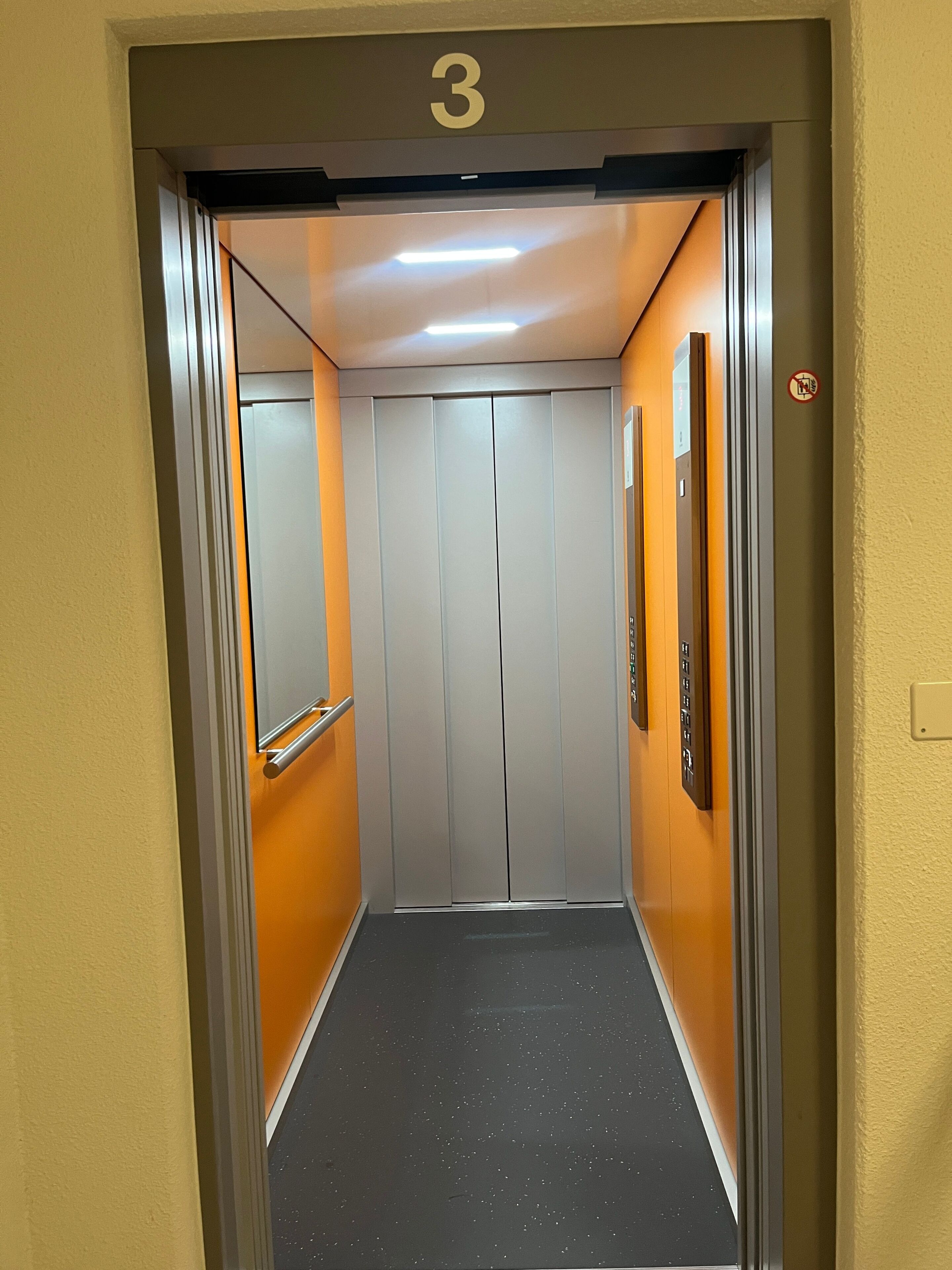 An elevator with a number '3' sign, a handrail, and a 'No Smoking' sign.