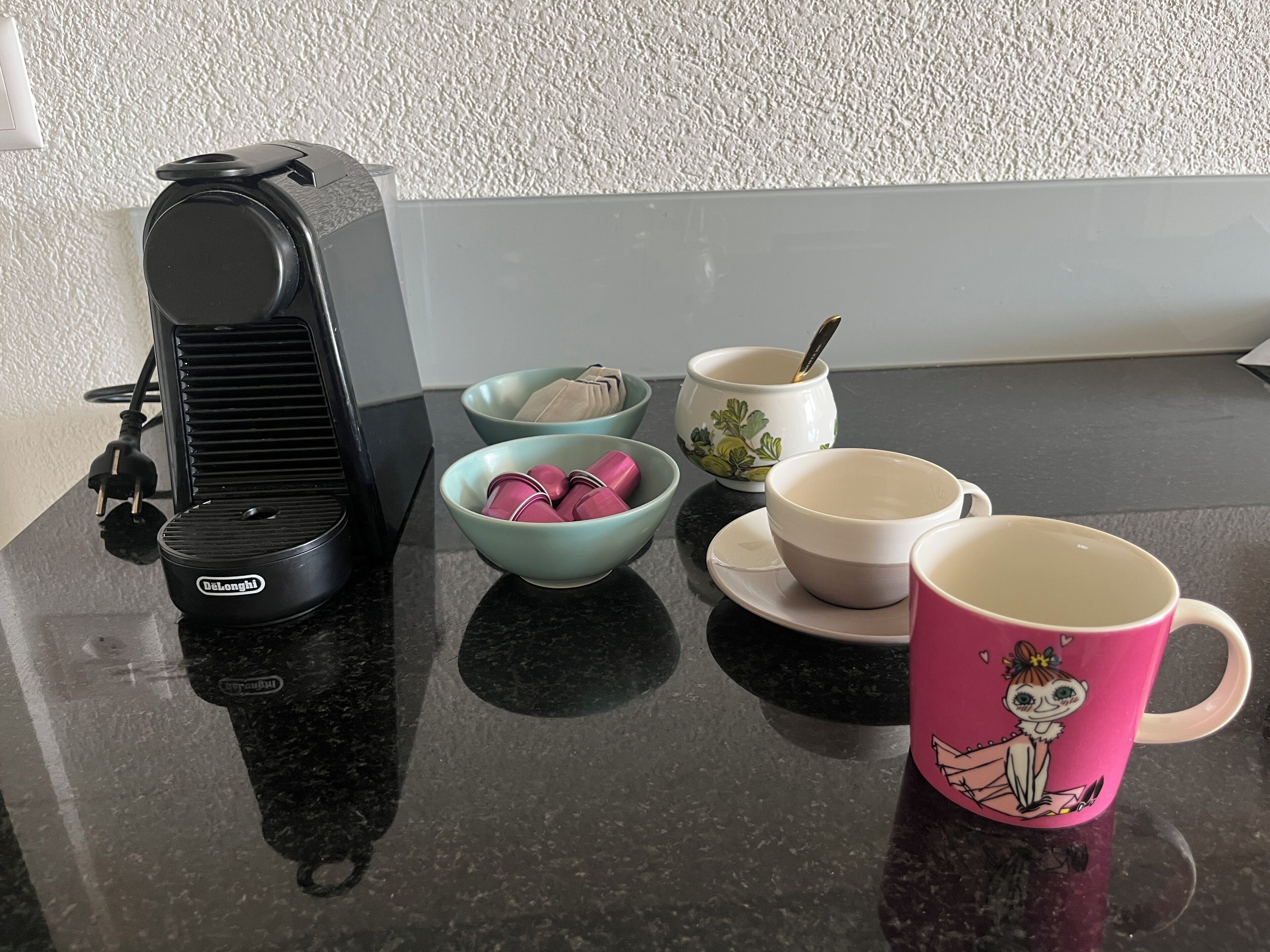 A kitchen counter with a coffee maker, bowls, a mug, and a spoon.