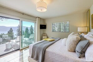 A hotel room with a large bed, a TV, a balcony with a view of trees and mountains, and a sliding glass door. - Stunning Lake & Mtn Views! CB/Incline Village Home (Crystal Bay)