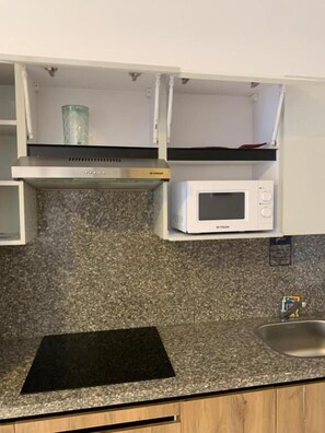 A kitchen with a microwave, a black countertop, and a stainless steel sink. - La prestigia Hurghada Apartment (Red Sea Governorate)