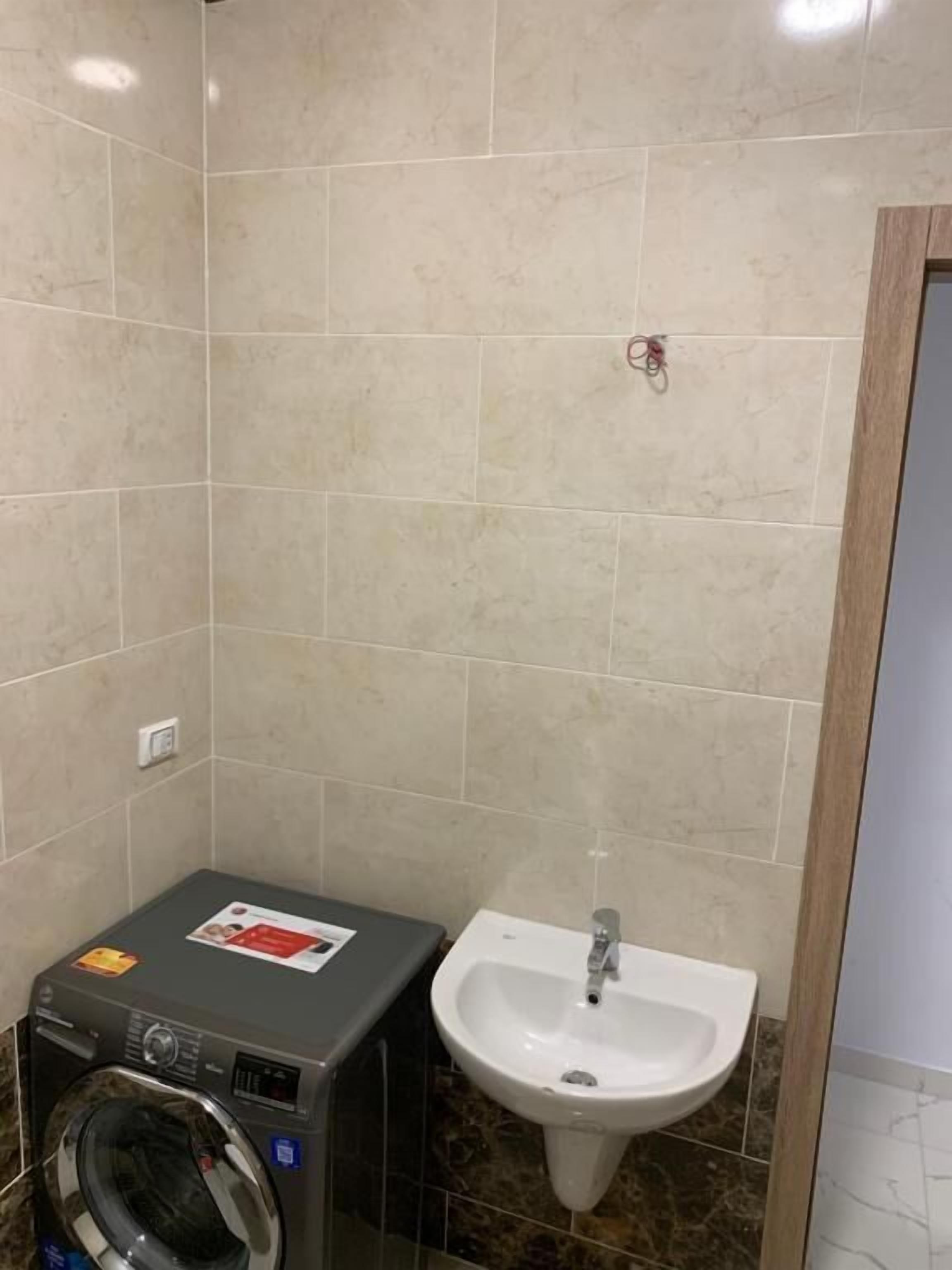 Une salle de bain équipée d’un lave-linge, d’un évier et de murs carrelés.