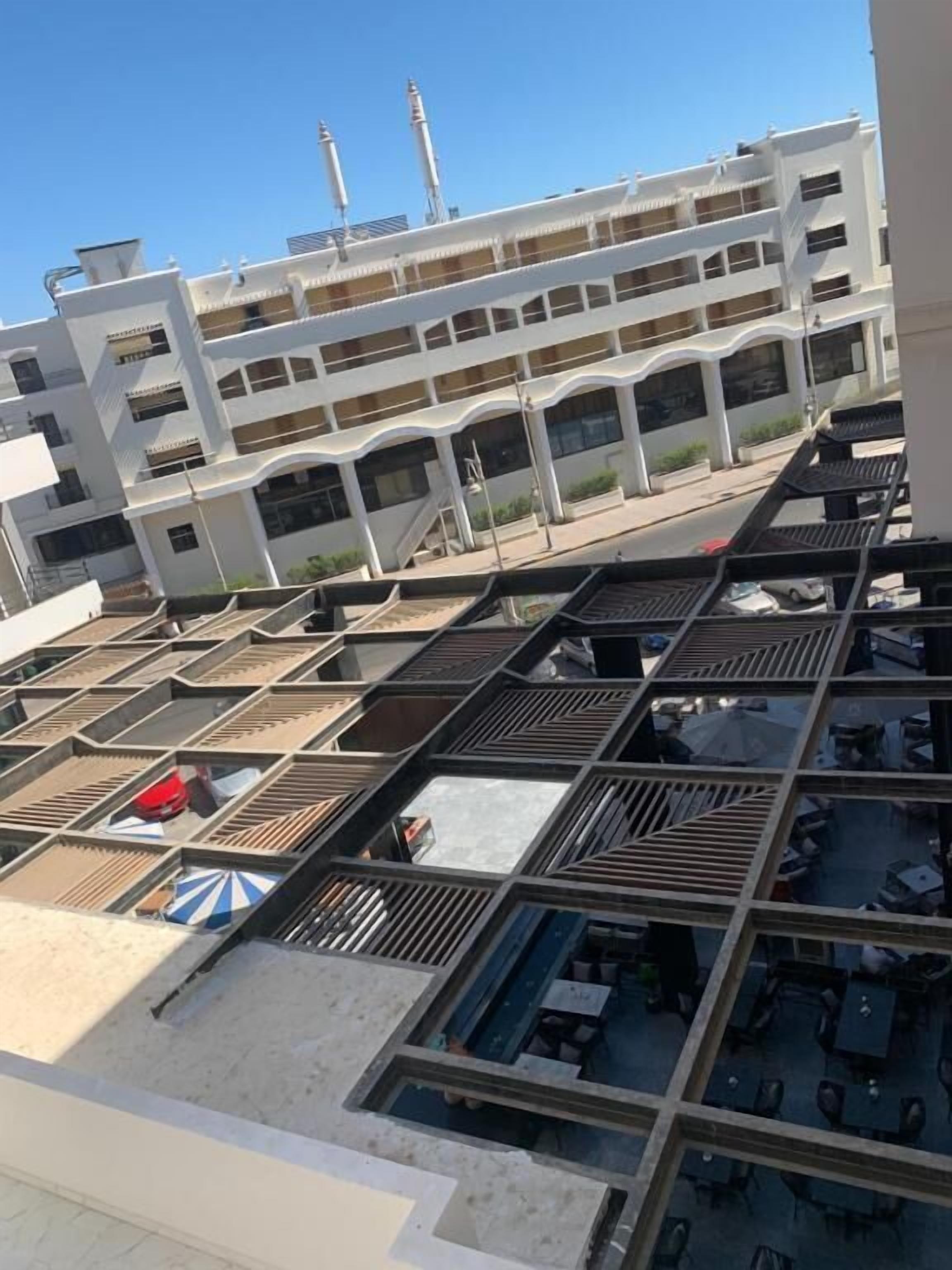 Un hotel de varios pisos con una terraza en la azotea que ofrece asientos al aire libre y vistas a un edificio blanco con minaretes.
