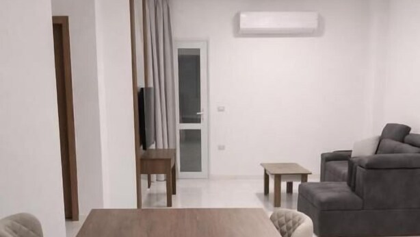A modern living room with a wooden dining table, a grey sofa, and a TV. - La prestigia Hurghada Apartment (Red Sea Governorate)