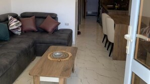 A modern living room with a sectional sofa, a small wooden coffee table, and a kitchen area visible through an open door. - La prestigia Hurghada Apartment (Red Sea Governorate)