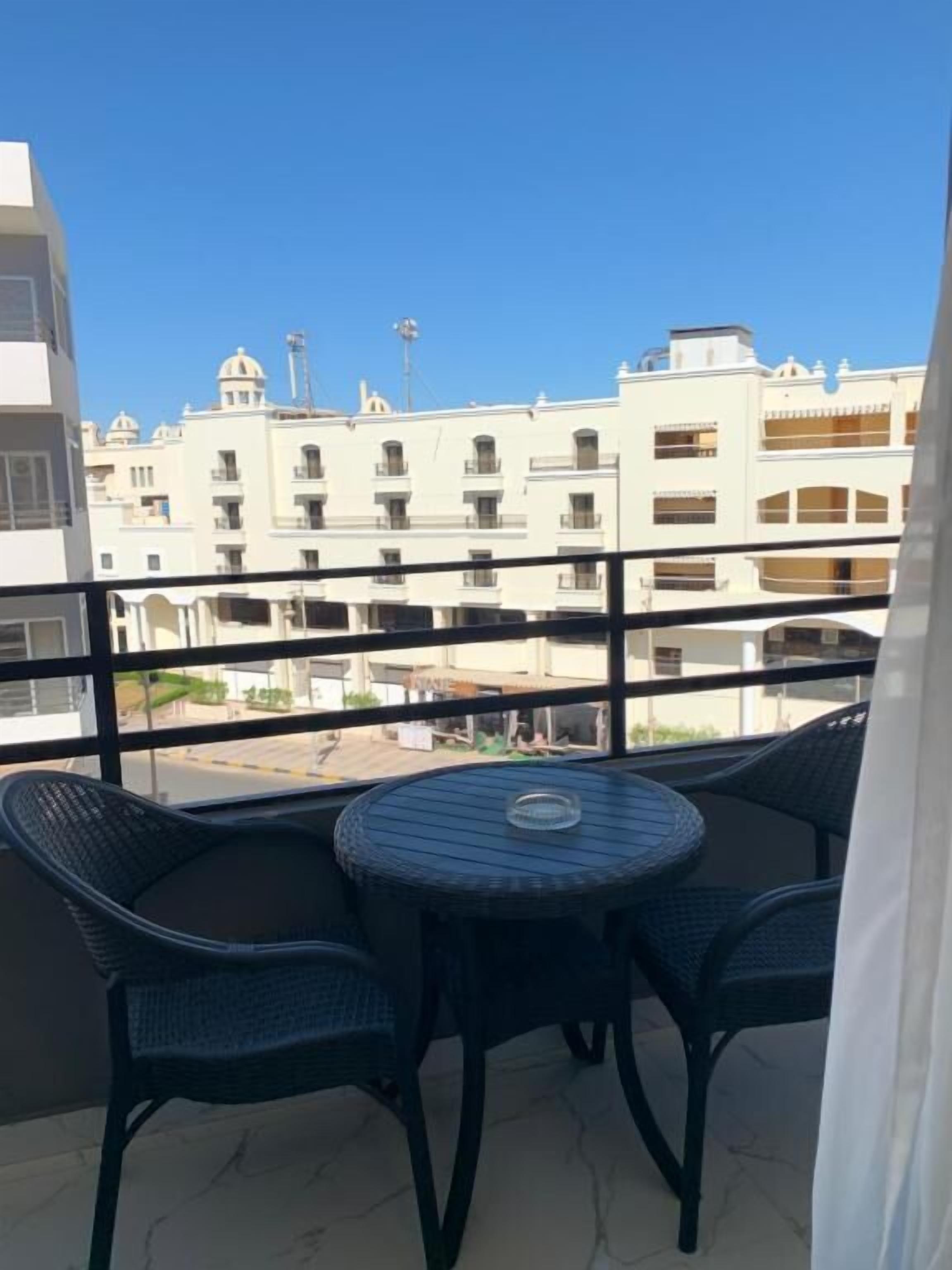 Un balcon avec une table ronde et deux chaises, donnant sur un paysage urbain avec des immeubles.