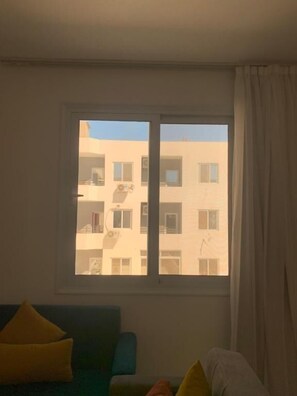 A room with a large window, a blue sofa, and a white chair. - La prestigia Hurghada Apartment (Red Sea Governorate)