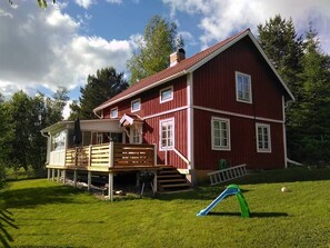 A red two-story house with a wooden deck and a slide.