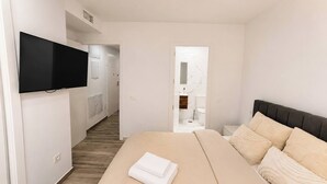 A hotel room with a bed, a television mounted on the wall, and a bathroom visible through an open door. - Playa del Cura Spa Retreat (Torrevieja)