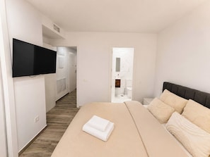 Ein Hotelzimmer mit Bett, einem an der Wand montierten Fernseher und einem durchgegangenen Tür einsehbaren Badezimmer.