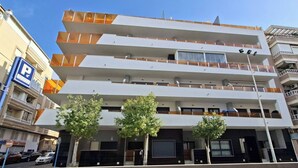 A multi-story building with balconies, a parking sign, and trees in front. - Playa del Cura Spa Retreat (Torrevieja)