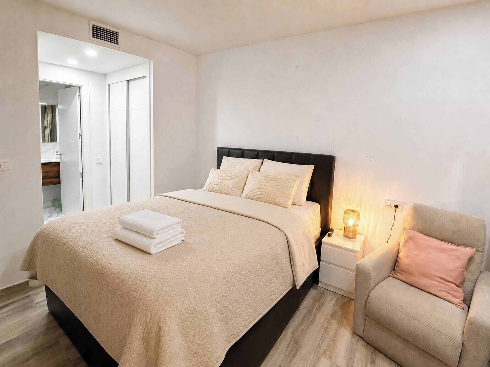 Een slaapkamer met een bed, nachtkastjes, een stoel en een nachtkastje met een lamp.