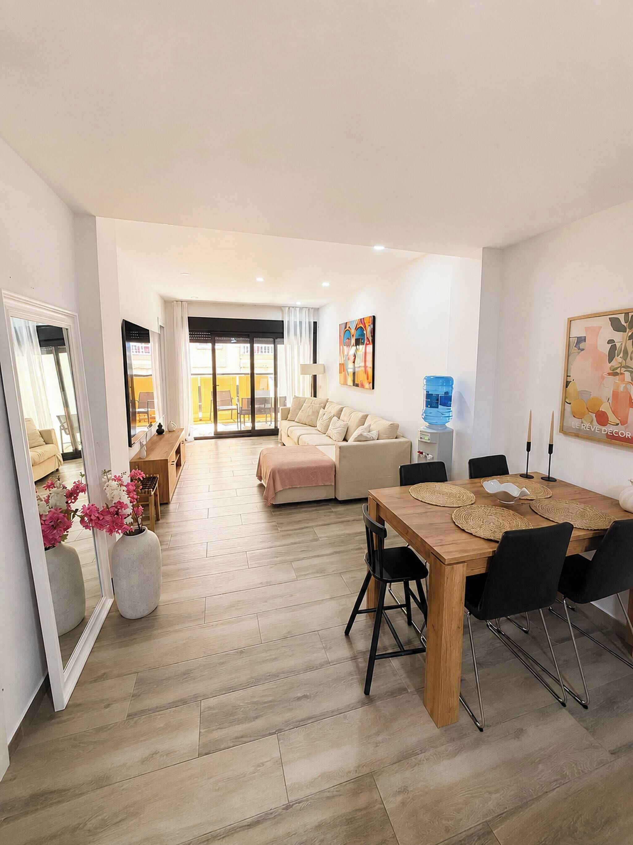A modern living room with a sofa, a dining table with chairs, and a kitchen area in the background.