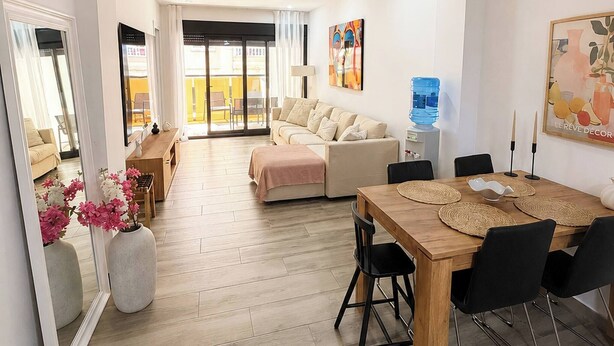A modern living room with a sofa, a dining table with chairs, and a large mirror reflecting the room. - Playa del Cura Spa Retreat (Torrevieja)